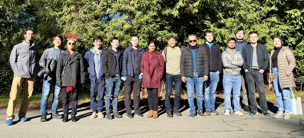 Image of lab group members lined up in front of some foliage, smiling.